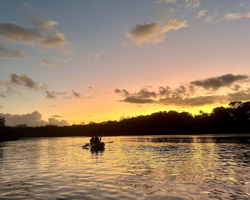 A double kayak alone on the river under an orange sunset sky